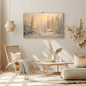 May include: A painting of a snowy forest scene with a small cabin in the distance. The painting is framed in a light wood frame and is hanging on a white wall. The painting is surrounded by a variety of decor, including a wicker chair, a coffee table, and a vase of dried pampas grass.