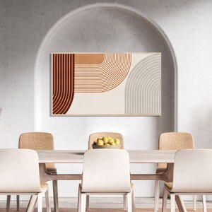 May include: A dining room with a white wall and a large archway. A framed abstract print with brown, orange, and gray geometric shapes hangs on the wall. A wooden table with six chairs is in the center of the room. A bowl of lemons sits on the table.