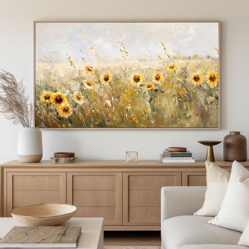 May include: A painting of a field of sunflowers in a light blue sky with white clouds. The sunflowers are yellow with brown centers and are in various stages of bloom. The field is green with tall grass and some brown stalks. The painting is framed in a light wood frame.