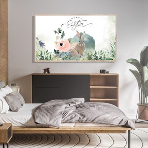 May include: A watercolor painting of a bunny rabbit with a pink flower and green leaves. The text "Happy Easter" is written in cursive above the bunny. The painting is framed and hanging on a wall in a bedroom.