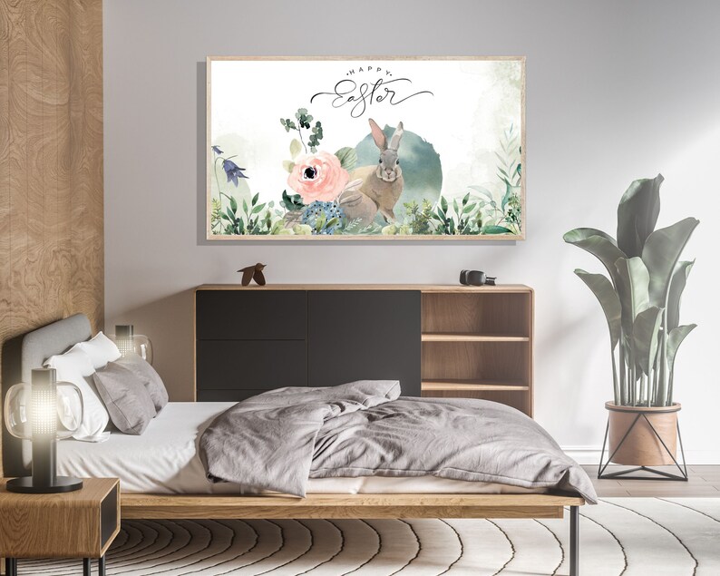 May include: A watercolor painting of a bunny rabbit with a pink flower and green leaves. The text "Happy Easter" is written in cursive above the bunny. The painting is framed and hanging on a wall in a bedroom.
