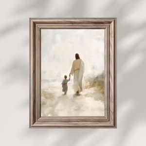 May include: Framed art print depicting a figure in a white robe holding hands with a child, walking on a sandy path. The artwork has a soft, muted color palette with a light brown wooden frame.