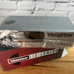 May include: A silver VistaView 110 Camera in its original packaging. The camera is wrapped in clear plastic and sits atop a red and black box with the camera's name printed on it.