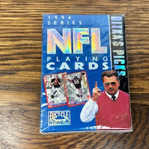 Pode incluir: Um baralho azul de cartas de jogar da NFL da s&eacute;rie de 1994, com um treinador de futebol e dois jogadores. O baralho &eacute; da cole&ccedil;&atilde;o Bicycle Sport e inclui o texto "Ditka's Picks".