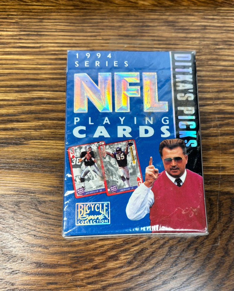 Pode incluir: Um baralho azul de cartas de jogar da NFL da s&eacute;rie de 1994, com um treinador de futebol e dois jogadores. O baralho &eacute; da cole&ccedil;&atilde;o Bicycle Sport e inclui o texto "Ditka's Picks".