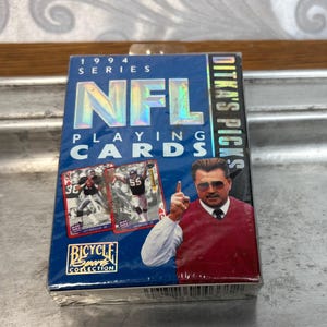 Pode incluir: Um baralho selado de cartas da NFL da s&eacute;rie de 1994. A caixa azul apresenta o logotipo da NFL, o texto "Ditka's Picks" e imagens de jogadores de futebol americano. O logotipo da Bicycle Sport Collection tamb&eacute;m &eacute; vis&iacute;vel.