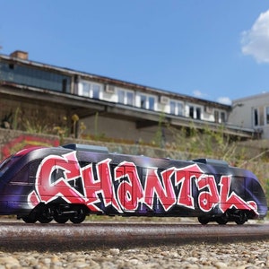 Op de afbeelding: Een zwarte en paarse trein met graffitikunst met het woord "CHANTAL" in rode en witte letters. De trein staat op een set roestige rails.