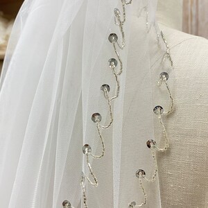 May include: White bridal veil with a beaded edge and silver sequins. The veil is made of soft tulle and has a delicate, romantic look.