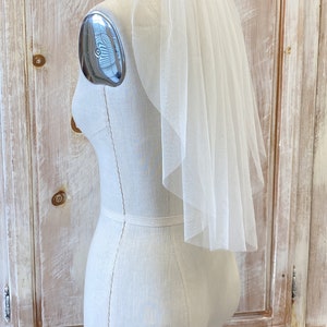 Puede incluir: Un velo de novia blanco de una sola capa con un borde festoneado, mostrado en un maniqu&iacute; blanco.