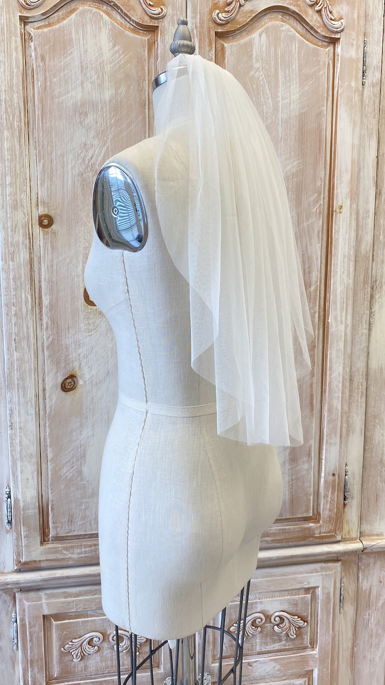 Puede incluir: Un velo de novia blanco de una sola capa con un borde festoneado, mostrado en un maniqu&iacute; blanco.