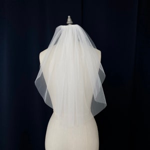 Puede incluir: Un velo de novia blanco de una sola capa con un borde festoneado. El velo est&aacute; hecho de tul suave y est&aacute; sujeto a un peine.