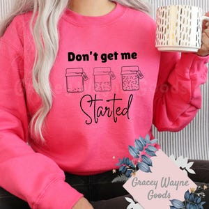 May include: Pink sweatshirt with the text "Don't get me started" and three jars with lids. The jars have a bubbly liquid inside and a tag on each lid that says "Get me started".