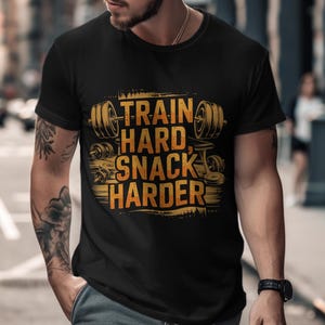 May include: Black t-shirt with a gold graphic that says "Train Hard, Snack Harder" with weightlifting imagery.