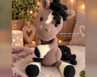 May include: A crocheted plush horse toy in light brown with a white blaze on its face, black mane, black tail, and white lower legs with black hooves. The toy features large dark eyes and the text made by nalucaDesign printed on its side.