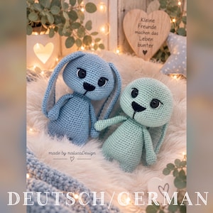 Puede incluir: Dos animales de peluche tejidos a mano, uno azul y otro verde menta, con orejas largas, ojos de seguridad negros y narices bordadas. El texto "made by nalucaDesign" es visible cerca de la base de la figura del conejo azul.