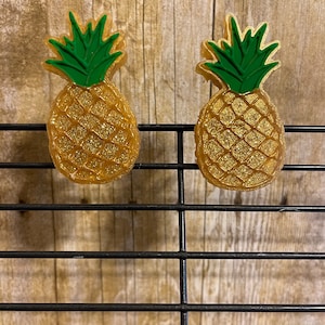 May include: Two gold glitter pineapple shaped hair clips with green leaves.