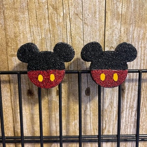 May include: Two black and red Mickey Mouse head-shaped ornaments with yellow eyes. The ornaments are made of foam and have a glittery finish.