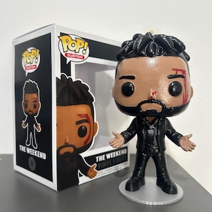 Può includere: Una statuetta in vinile personalizzata di The Weeknd, con un abito nero, barba e acconciatura. La statuetta presenta una piccola ferita sul viso. La statuetta è esposta accanto alla sua scatola, con il logo Pop! Custom e la scritta "The Weeknd".