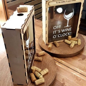 May include: Two wooden wine bottle holders with a glass pane and cork stoppers. The holders have the text "Oh! It's Wine O'Clock!" printed on them.