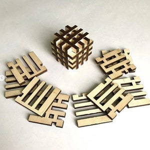 Könnte beinhalten: Ein Holzpuzzle mit einer Würfelform und acht separaten Teilen. Der Würfel ist aus dunklem Holz und die Teile sind aus hellem Holz. Die Teile sind in Form eines Gitters mit einem Muster aus Quadraten und Rechtecken.