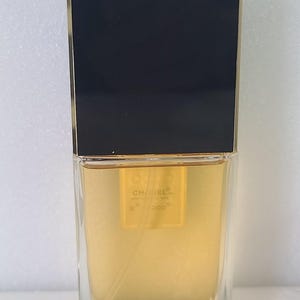 K&ouml;nnte beinhalten: Ein rechteckiger Parf&uuml;mflakon mit schwarzem Deckel und goldenen Akzenten. Die transparente Glasflasche enth&auml;lt eine goldfarbene Fl&uuml;ssigkeit. Der Markenname "CHANEL" und "COCO" sind sichtbar.