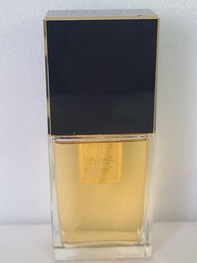 K&ouml;nnte beinhalten: Ein rechteckiger Parf&uuml;mflakon mit schwarzem Deckel und goldenen Akzenten. Die transparente Glasflasche enth&auml;lt eine goldfarbene Fl&uuml;ssigkeit. Der Markenname "CHANEL" und "COCO" sind sichtbar.