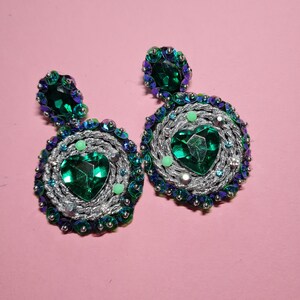 Puede incluir: Un par de pendientes de declaraci&oacute;n plateados y verdes con piedras grandes en forma de coraz&oacute;n verde y piedras verdes m&aacute;s peque&ntilde;as que rodean las piedras m&aacute;s grandes.