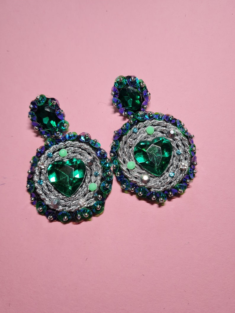 Puede incluir: Un par de pendientes de declaraci&oacute;n plateados y verdes con piedras grandes en forma de coraz&oacute;n verde y piedras verdes m&aacute;s peque&ntilde;as que rodean las piedras m&aacute;s grandes.