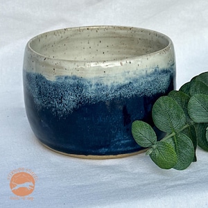 May include: A handmade ceramic bowl with a speckled white rim and a deep blue glaze that fades into the white. The bowl has a rounded shape and a smooth finish. The bowl is approximately 4 inches in diameter and 3 inches tall.