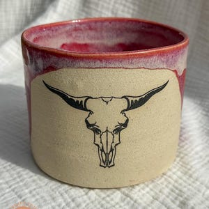 Può includere: Una tazza di ceramica bianca con manico nero e la scritta "But First, Coffee" in nero, con un font in stile scritto a mano. La tazza è su una superficie bianca.