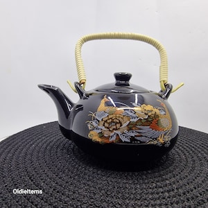 May include: Black ceramic teapot with a bamboo handle and a gold and white design of peacocks and flowers.