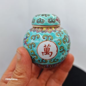 May include: A small, blue and white porcelain jar with a lid. The jar is decorated with a repeating pattern of yellow and green swirls. The lid has a similar pattern and a red Chinese character on top.