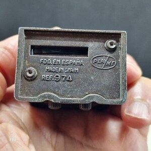 May include: A small, rectangular, silver-toned metal toy radio with a slot and two knobs. The text "FDO. EN ESPA&Ntilde;A MADE IN SPAIN REF. 974" is stamped on the surface, along with the "PLAY ME" logo.