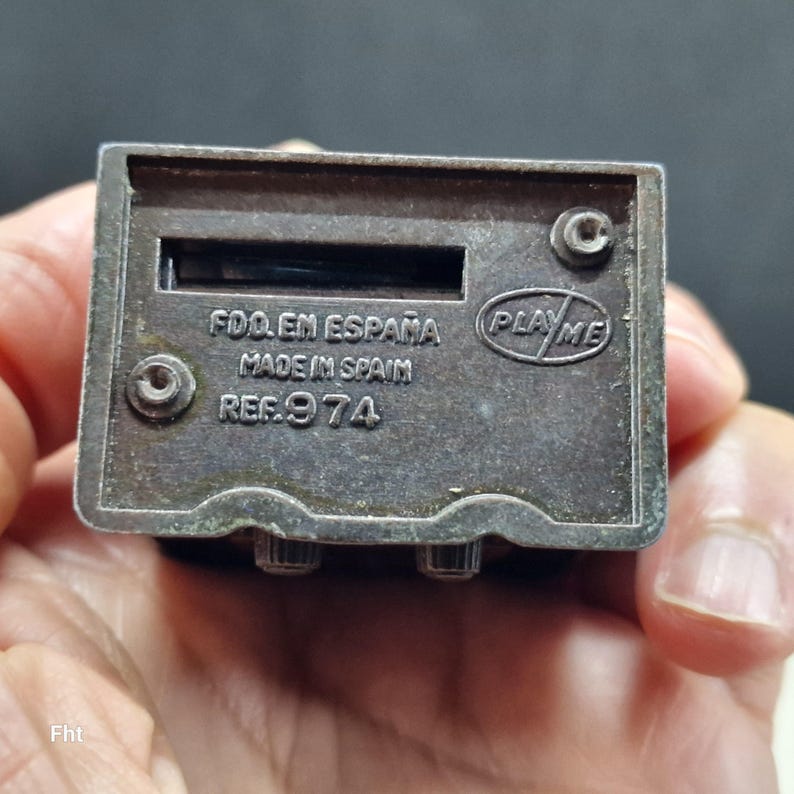 May include: A small, rectangular, silver-toned metal toy radio with a slot and two knobs. The text "FDO. EN ESPA&Ntilde;A MADE IN SPAIN REF. 974" is stamped on the surface, along with the "PLAY ME" logo.