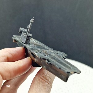 May include: A detailed model of a warship, primarily dark gray with visible weathering. The model features a detailed superstructure, including a mast and radar array. The ship's deck shows intricate detailing, suggesting a miniature replica of a naval vessel.