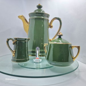 Könnte beinhalten: Ein grünes und goldenes Teeservice mit Teekanne, Milchkännchen und Zuckerdose. Das Set ist aus Keramik und hat einen goldenen Rand.