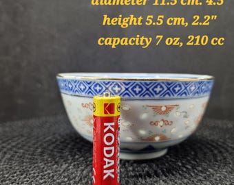 May include: A small, decorative porcelain bowl with a blue and white geometric pattern around the rim and a gold trim. The bowl is 11.5 cm in diameter and 5.5 cm high. A red Kodak battery is in front of the bowl.