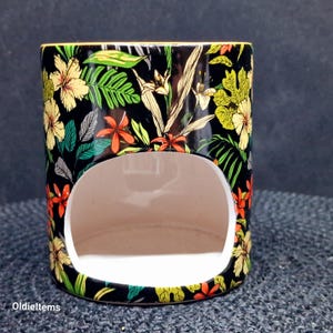 May include: Black ceramic wax melt warmer with a floral design featuring yellow, red, and green flowers. The warmer has a cut-out for a tea light.
