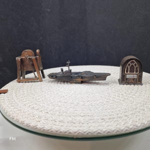 May include: Miniature metal sculptures of a ship, a radio, and a grinding wheel. The ship is dark gray with a small tower. The radio is brown with a decorative arched window. The grinding wheel is brown with a circular wheel.