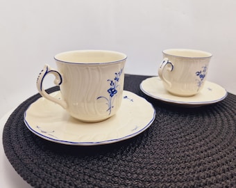 May include: Two white porcelain teacups with blue floral designs and matching saucers. The cups and saucers have a scalloped edge.