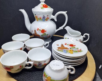 May include: A white porcelain tea set with a teapot, creamer, cups, and saucers. The set features a colourful Asian-inspired design with pagodas, figures, and floral accents. The teapot has a lid with a red floral design.