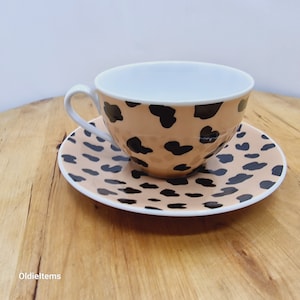 May include: A white teacup and saucer set with a brown and black leopard print design.