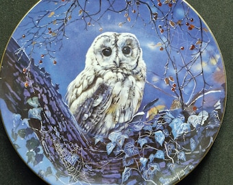 May include: A decorative plate with a painting of a white owl on a tree branch, set against a dark blue backdrop with branches, berries, and ivy. The plate has a gold rim and the artist's signature. A beautiful piece of art.