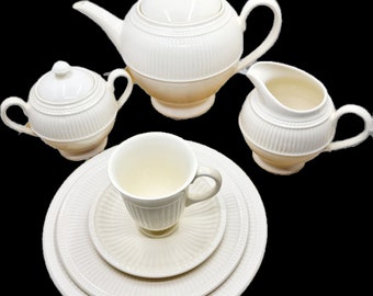May include: A white tea set with a teapot, creamer, sugar bowl, cup and saucer. The set has a ribbed design and is made of fine china.