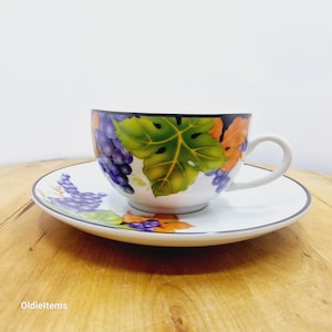 Peut inclure: Service à thé blanc avec un motif de raisin et de feuilles. La tasse à thé a un bord noir et une anse blanche. La soucoupe et la tasse à thé sont décorées de raisins violets, de feuilles vertes et d'accents orange.