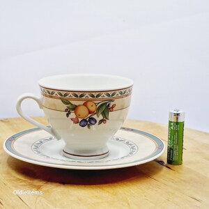 May include: A white teacup and saucer with a floral pattern featuring oranges, green leaves, and blue berries. The saucer has a teal border.