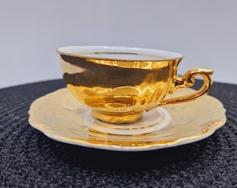 May include: A teacup and saucer set with a white base and gold accents. The cup and saucer have a delicate, scalloped edge.