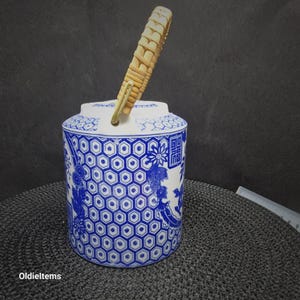 Può includere: Una teiera in ceramica bianca con un motivo floreale blu e bianco e un manico in bambù intrecciato. La teiera ha un motivo esagonale e caratteri cinesi.
