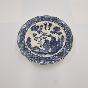 May include: A blue and white porcelain bowl with a traditional willow pattern. The bowl has a scalloped edge and a gold rim.