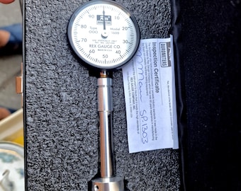 May include: A Rex Gauge Co. durometer, model 1600, in a black case. The dial gauge has a white face with black markings and a needle. An inspection certificate is included. The tool is made in the USA.